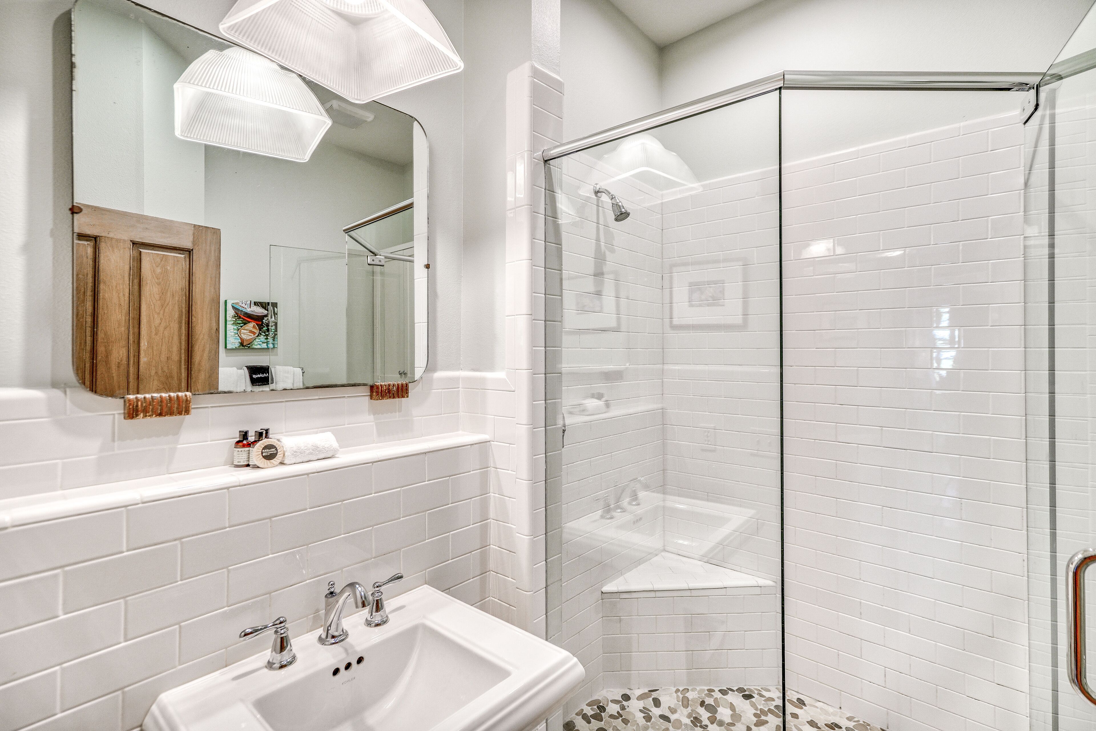 Un baño con lavamanos blanco, espejo y zona de ducha.
