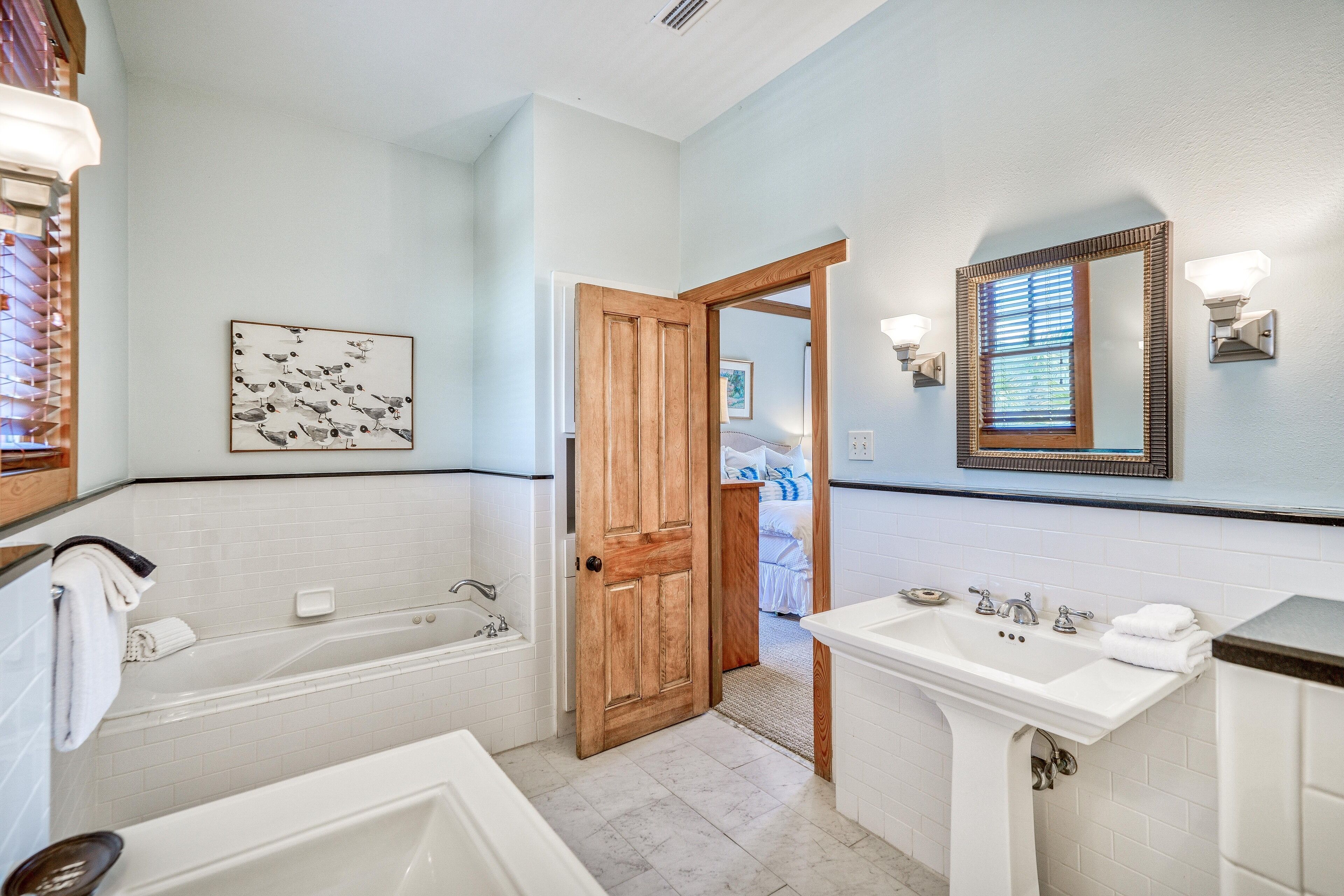 Un baño con bañera, lavabo y puerta de madera que da a un dormitorio.