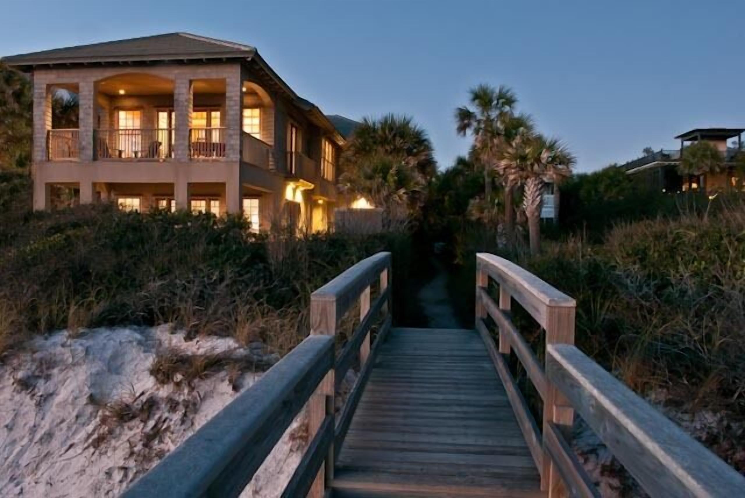 A beachfront property with a wooden deck leading to a building with multiple balconies.