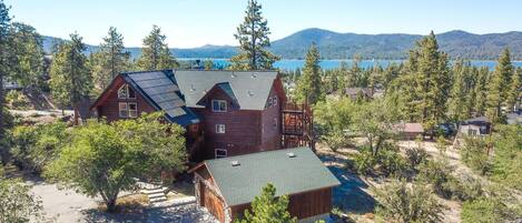 A large wooden cabin with a sloped roof, surrounded by trees and a lake in the background.
