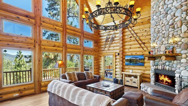 A log cabin interior with a fireplace, large windows, and a cozy seating area. - Grand Cameron Estate by Destination Big Bear : Movie Theater! HOT TUB! Lake Views! PET FRIENDLY 🐾!Walk to the Village! Game Room w/ Pool Table! (Big Bear Lake)