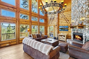 A log cabin interior with a fireplace, large windows, and a cozy seating area.