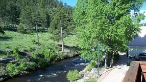A riverside walkway with a wooden bench, a metal railing, and a view of a river and forested area.