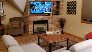 A living room with a stone fireplace, a television mounted on the wall, and a wooden ceiling.