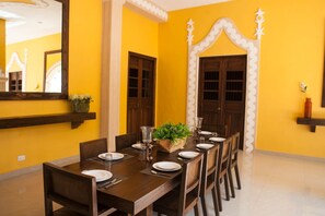 A dining area with a long wooden table set for six, flanked by two doors with decorative arches.