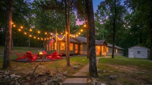 Une cabane avec une façade en pierre, un foyer, des chaises rouges et des guirlandes lumineuses.