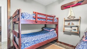 Un lit superposé avec une couvre-lit à motifs, une tête de lit en bois, une étagère avec des livres et un modèle de bateau, et un petit tapis sur le sol.
