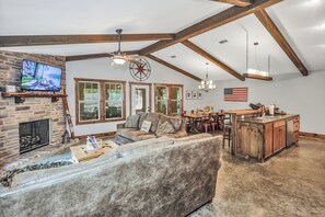 Ein geräumiges Wohnzimmer mit Kamin, Fernseher, einer großen Couch und einem Essbereich mit Holztisch und Stühlen.