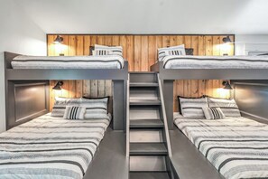Dormitorio con literas, cabecera de madera, dos lámparas de noche y una escalera central.