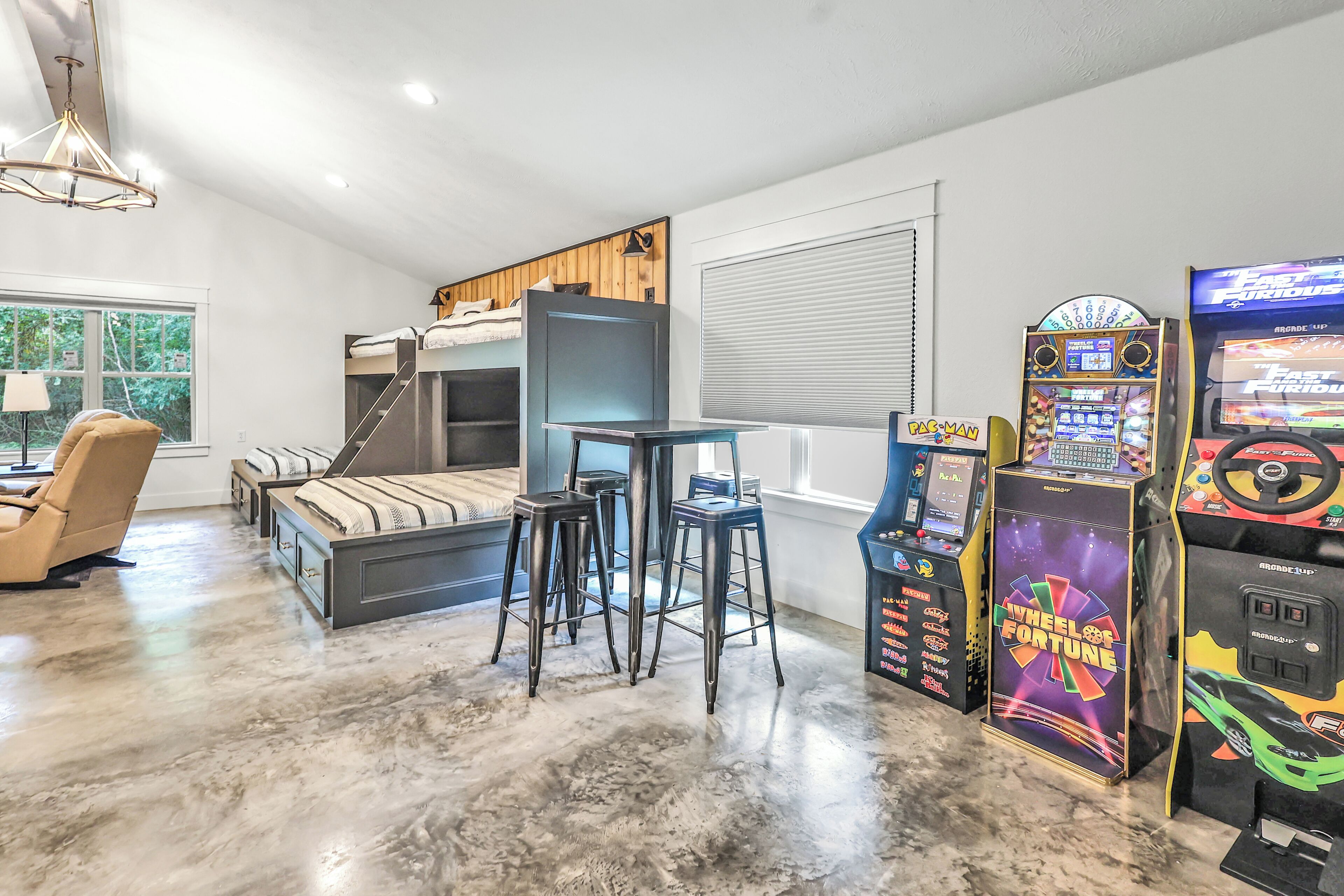 A modern bedroom with bunk beds, a desk, and arcade games.
