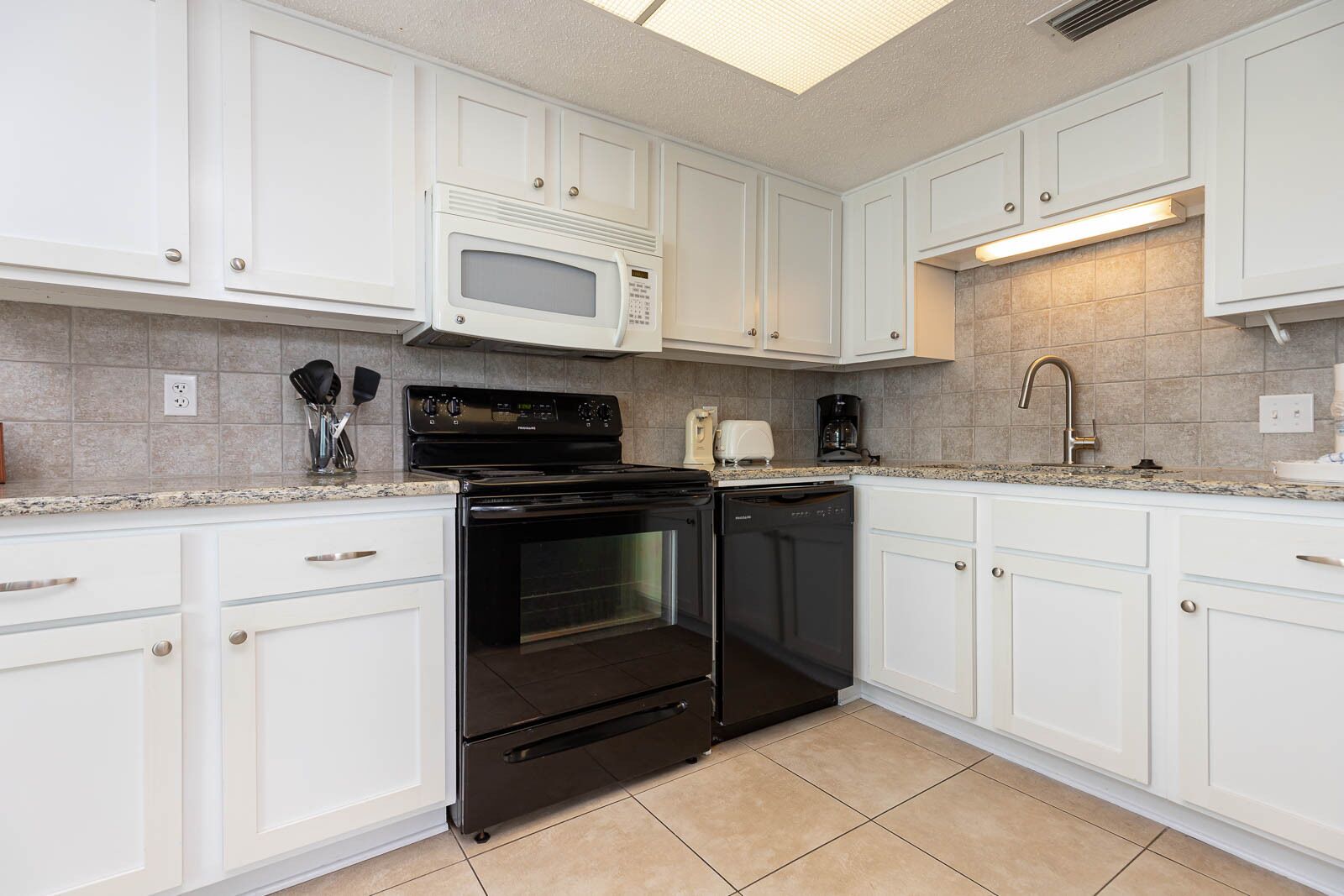 A kitchen with white cabinets, a black stove, a microwave, and a dishwasher.
