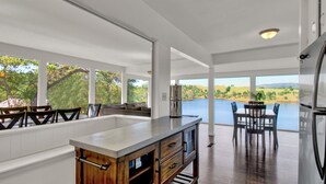 A modern kitchen with a large island, dining area, and a view of a lake. - Tulloch Lake House! Panoramic Views & Private Dock (Jamestown)