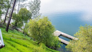 A grassy hillside with a dock extending into a calm lake, surrounded by trees. - Tulloch Lake House! Panoramic Views & Private Dock (Jamestown)