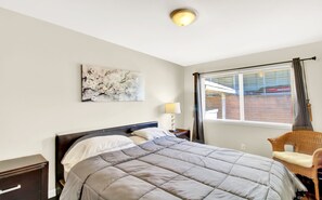 Un dormitorio con cama, mesita de noche, silla, ventana con cortinas e iluminación en el techo.