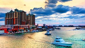 A waterfront hotel with multiple balconies, a marina with boats, and a cityscape in the background.
