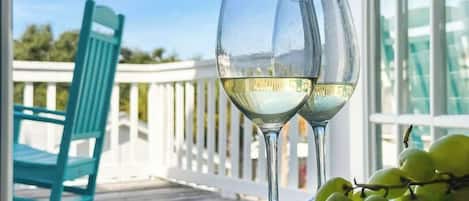 Two wine glasses on a table with a view of a white railing and a blue chair.