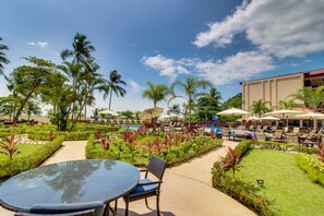 A resort pool area with lounge chairs and umbrellas, surrounded by palm trees and well-maintained lawns. - The Palms 703 (Jacó)