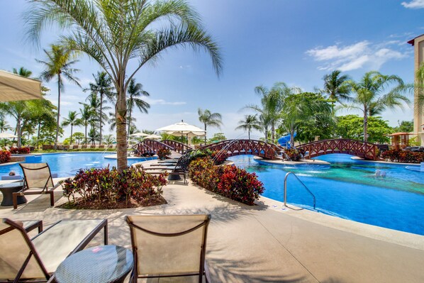 A pool area with lounge chairs, a bridge, and palm trees.