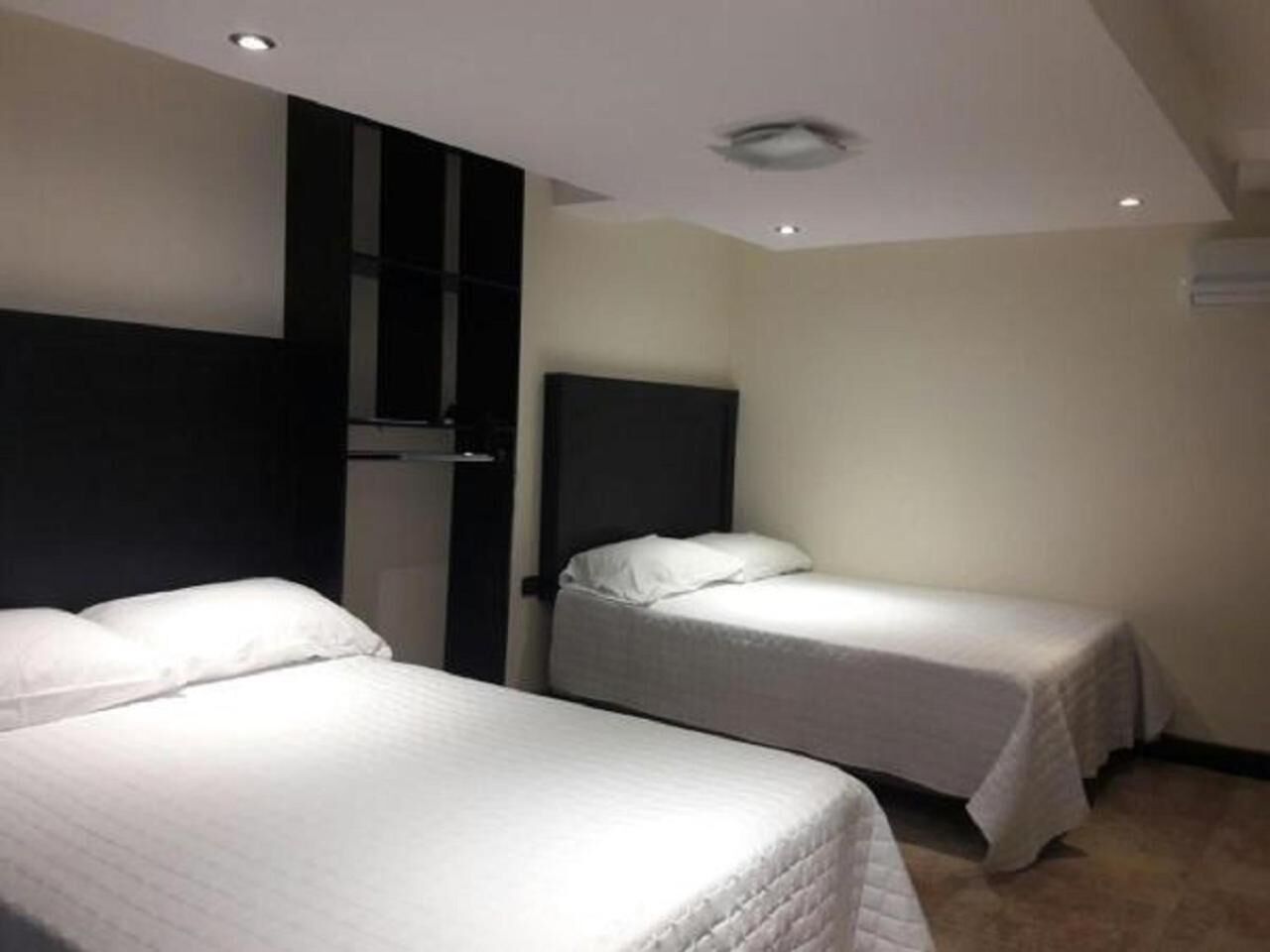 Una habitación de hotel con dos camas individuales, un cabecero oscuro y una pared blanca.