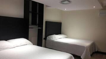 Una habitación de hotel con dos camas individuales, un cabecero oscuro y una pared blanca.