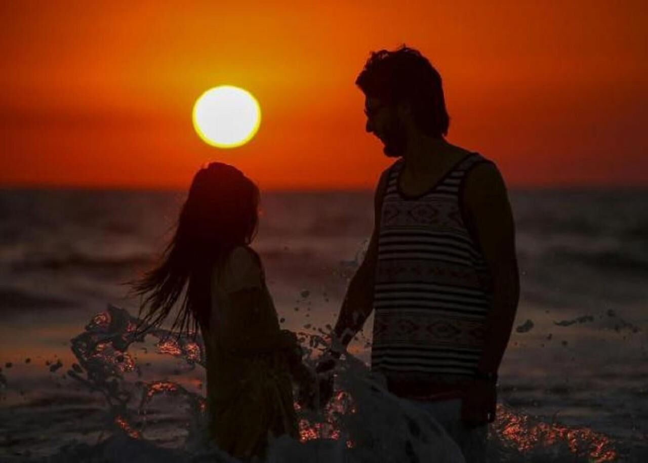 Un atardecer con una persona y un niño junto al agua.