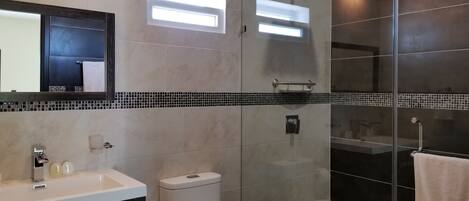 Un baño moderno con cabina de ducha de vidrio, inodoro, lavabo con espejo y salpicadero de azulejos.