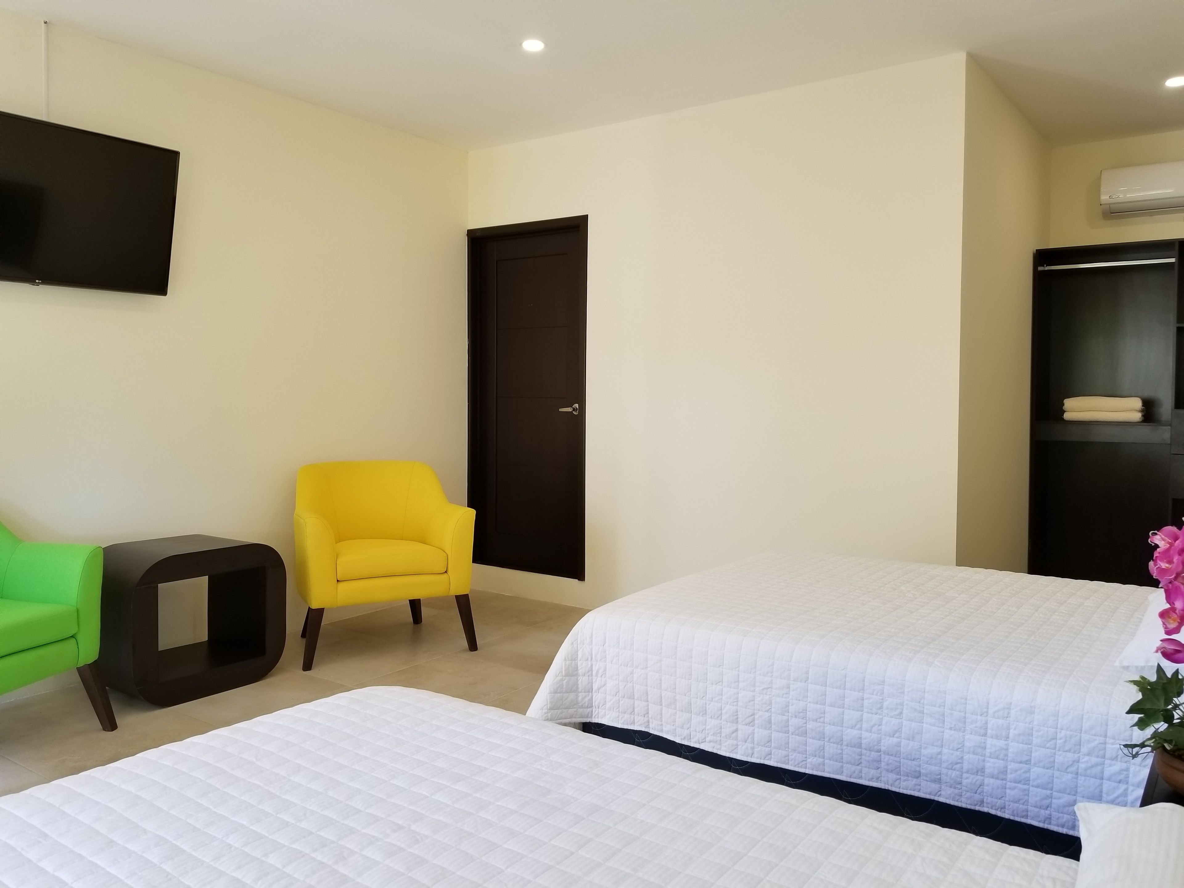 A hotel room with two beds, a TV mounted on the wall, a door, and a small table.