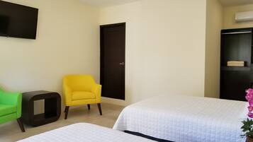 Habitación de hotel con dos camas, un televisor en la pared, una puerta y una mesita.