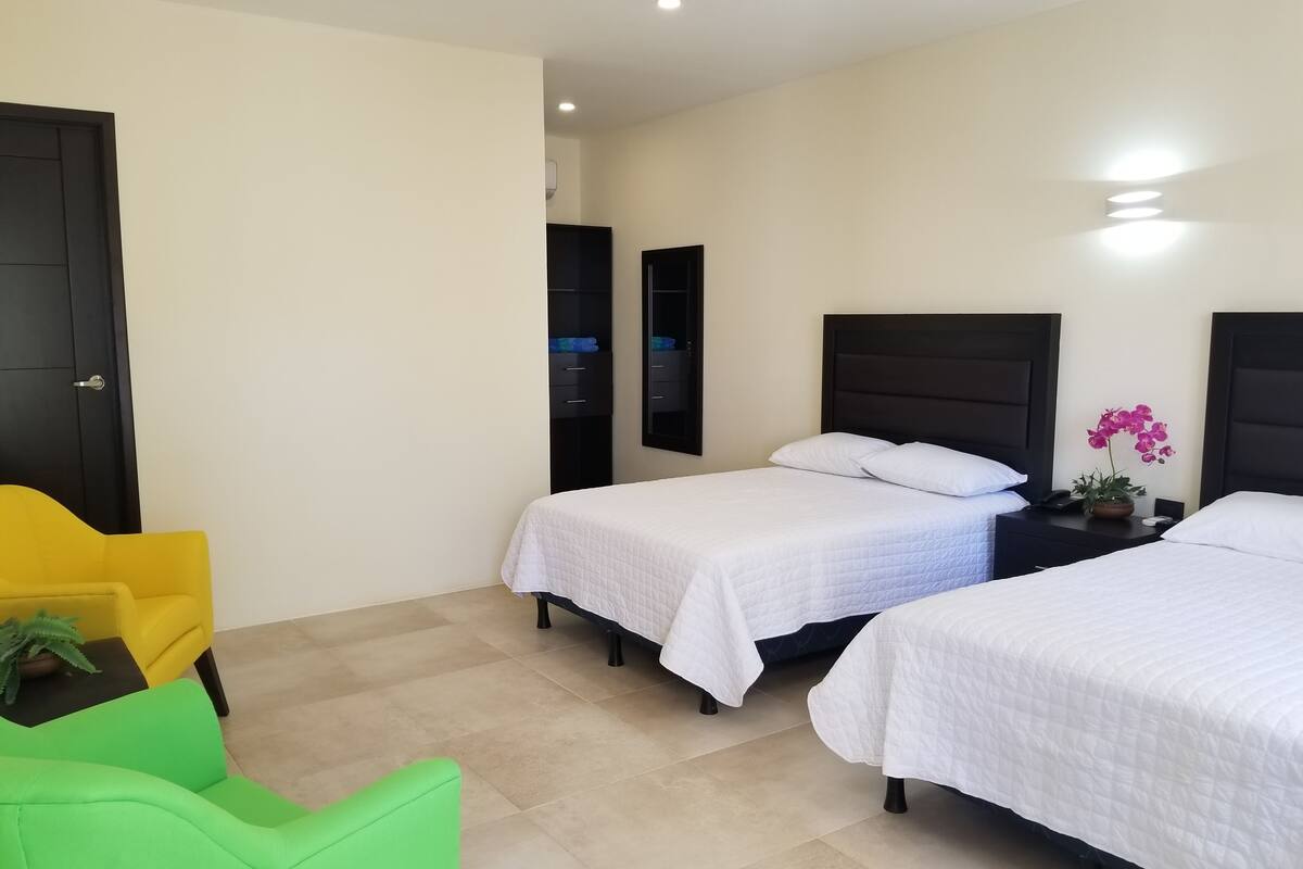 A hotel room with two beds, a yellow chair, and a green chair.