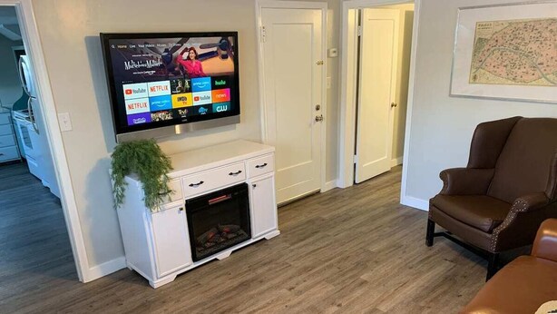 Ein Wohnzimmer mit flachbildfernseher an der Wand, Kamin, braunem Ledersessel und einer Couch.