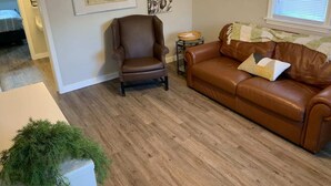 Ein Wohnzimmer mit einem braunen Ledersessel, einer braunen Ledersofa, einem kleinen runden Tisch mit einem Korb und einer gerahmten Karte an der Wand.