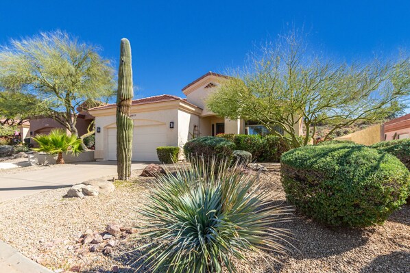 A residential area with a house, a tall cactus, and various shrubs. - Beautiful home w/ private heated pool in quiet gated community. (Mesa)