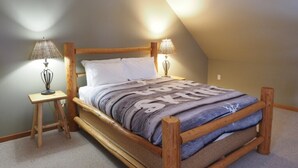 Een houten bed in een kamer met een schuine kap, twee bedlampen en een vloerbedekking.