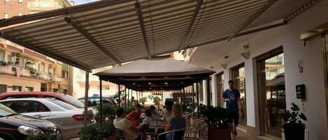 An outdoor patio with tables and chairs, surrounded by potted plants.