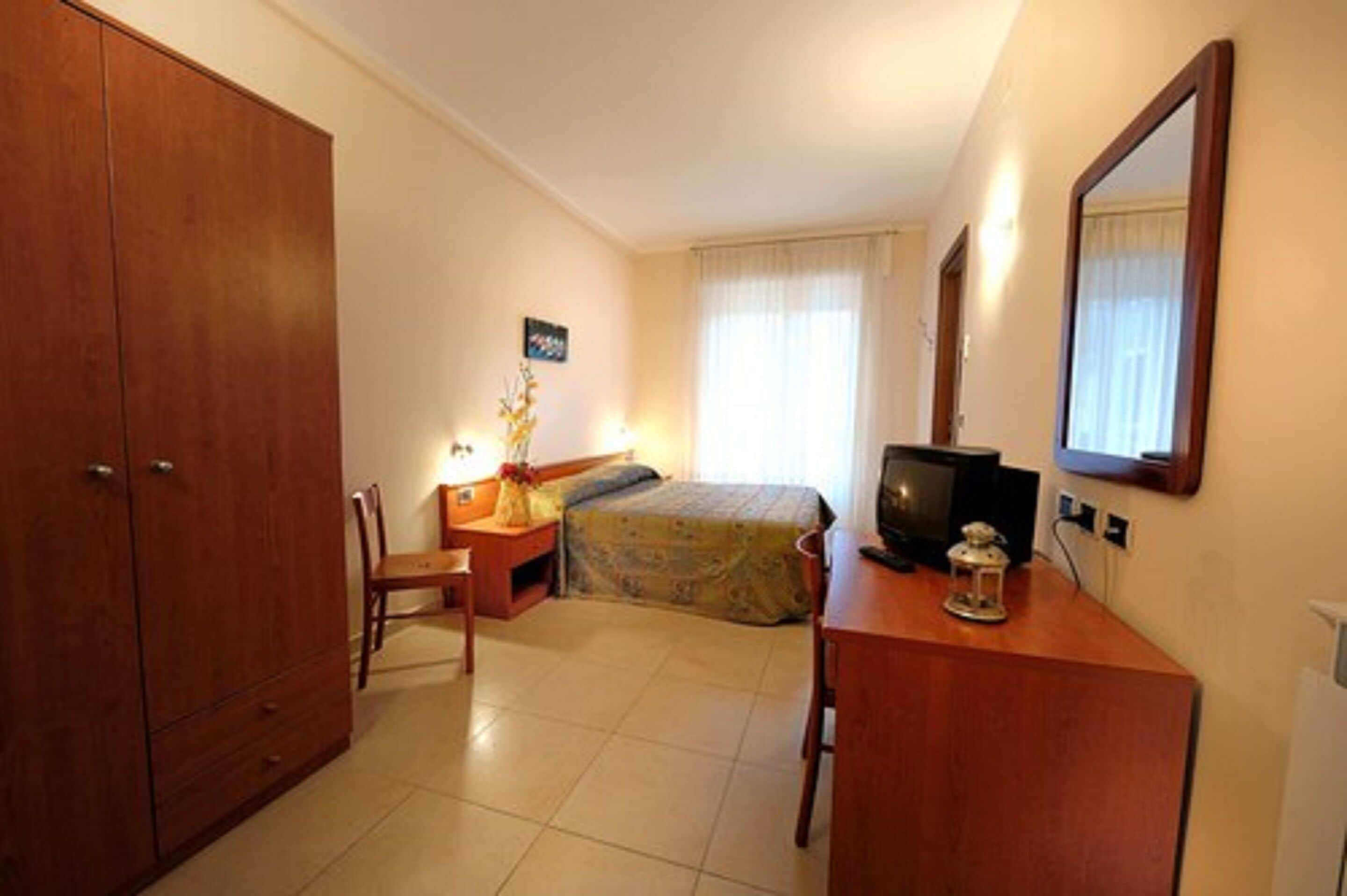 A hotel room with a bed, a desk, a chair, a wardrobe, a television, and a mirror.
