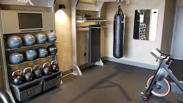 Une salle de sport équipée de kettlebells, d’un sac de frappe et d’un vélo d’appartement.