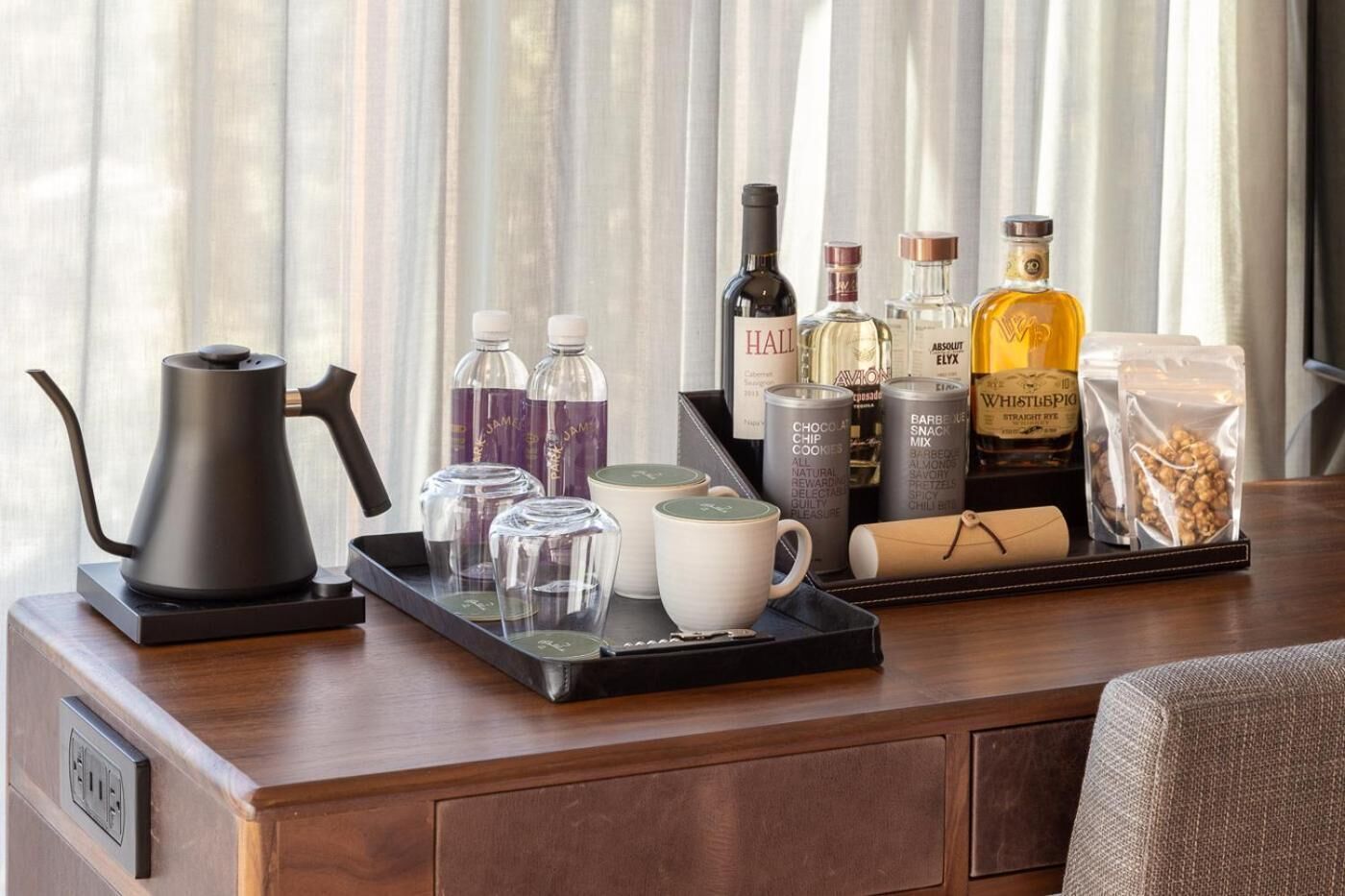 A tray with a coffee pot, glasses, and bottles of beverages on a wooden table.