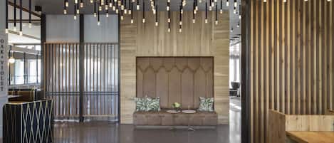 A modern interior with a wooden reception desk, a seating area with a sofa and two small tables, and a hanging light fixture.