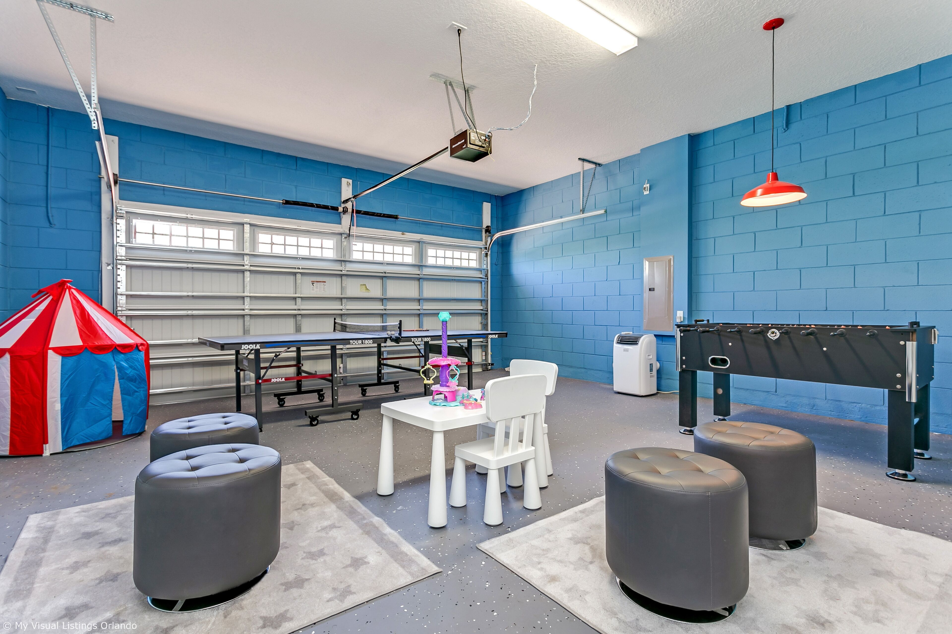 A room with a blue brick wall, a white table with chairs, a red and blue tent, and a pool table.