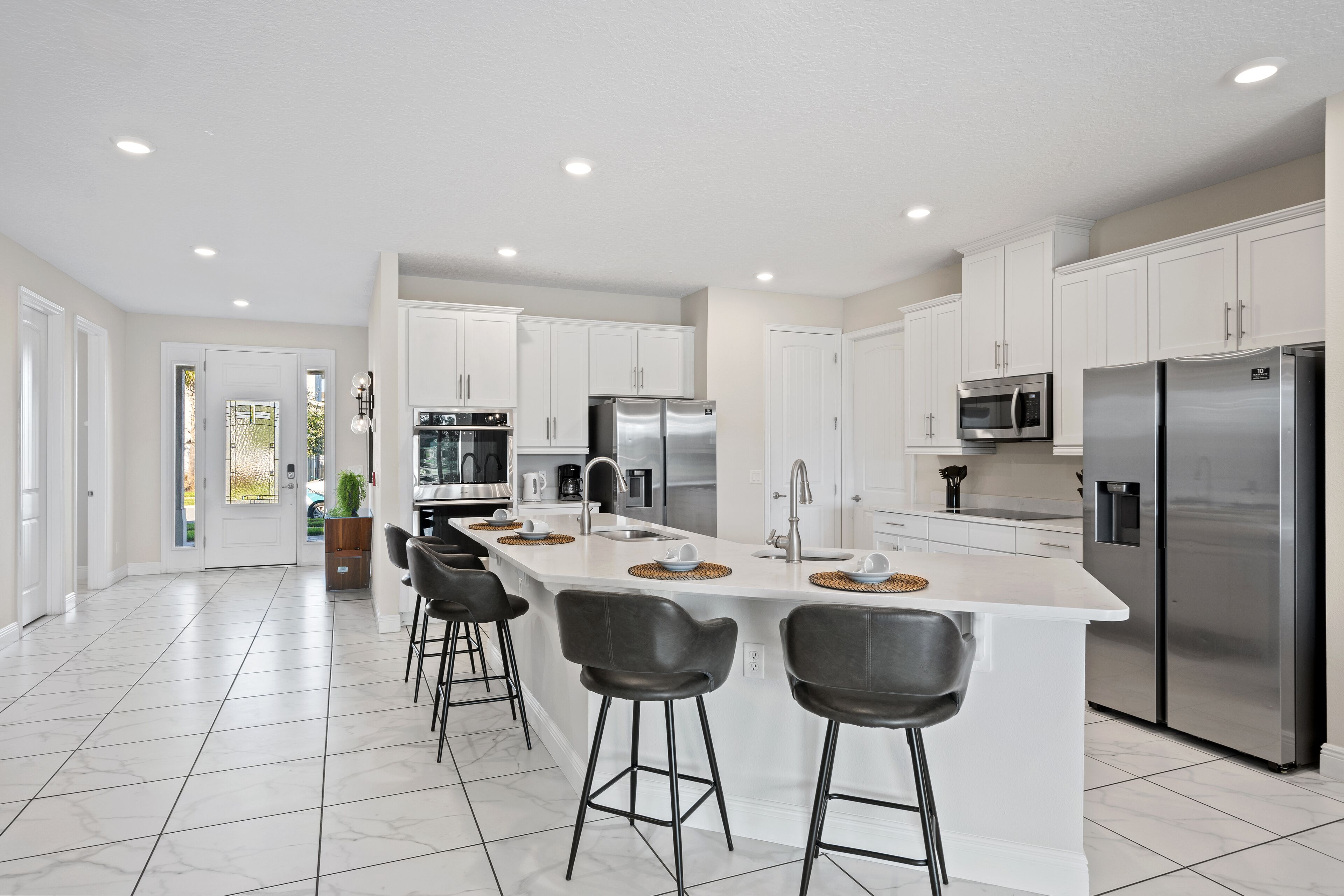 A modern kitchen with white cabinetry, stainless steel appliances, and a central island with bar stools.