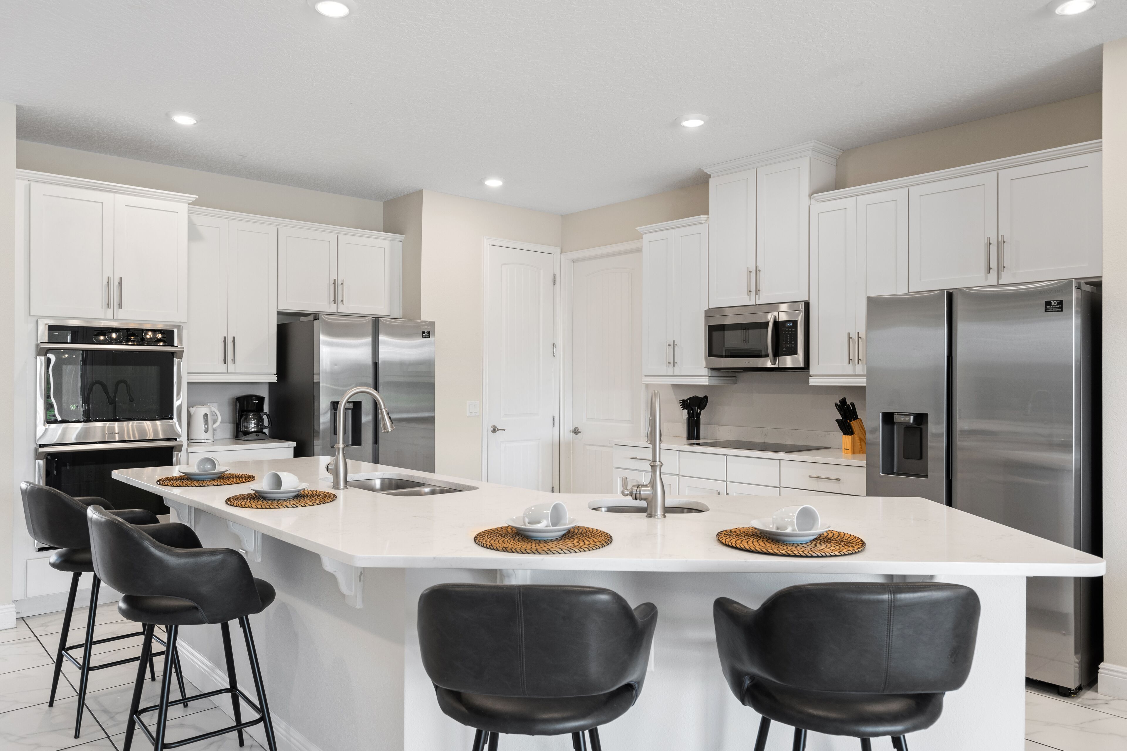 Una cocina moderna con armarios blancos, electrodomésticos de acero inoxidable, una isla central con taburetes y un microondas sobre la isla.