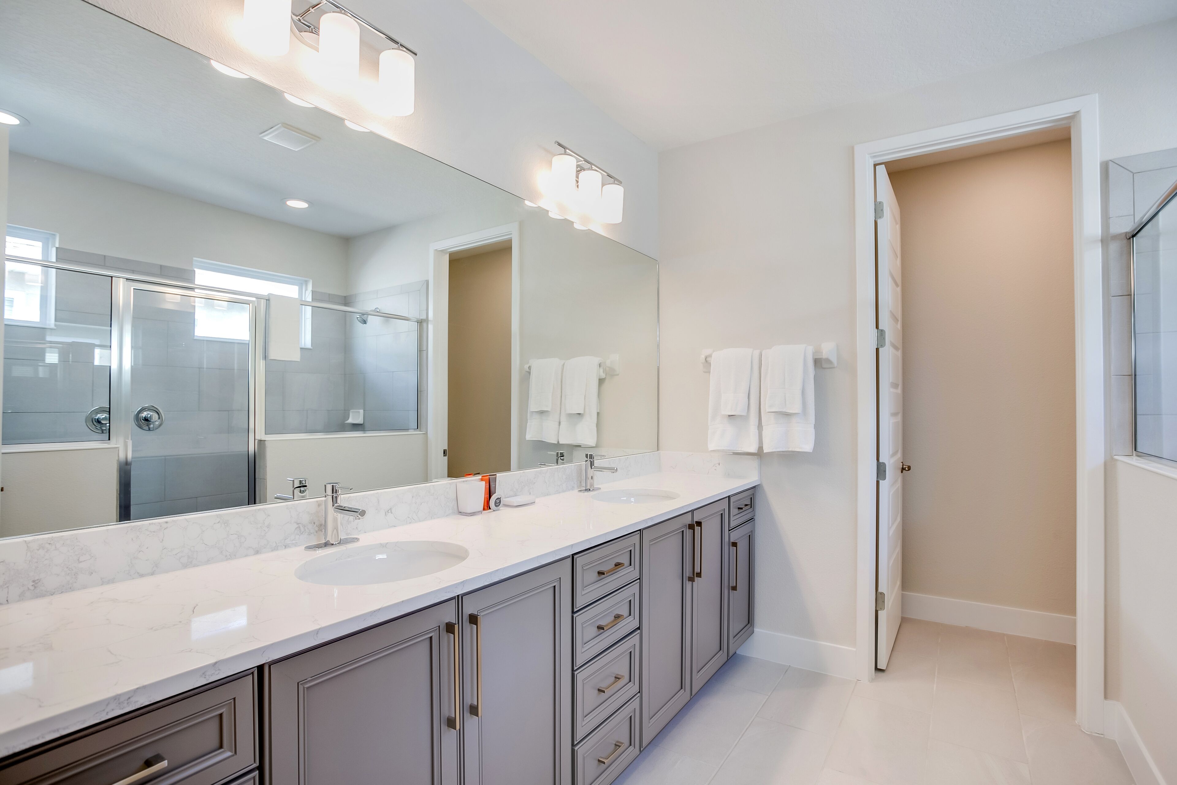A modern bathroom with a large mirror, two sinks, and a walk-in shower.