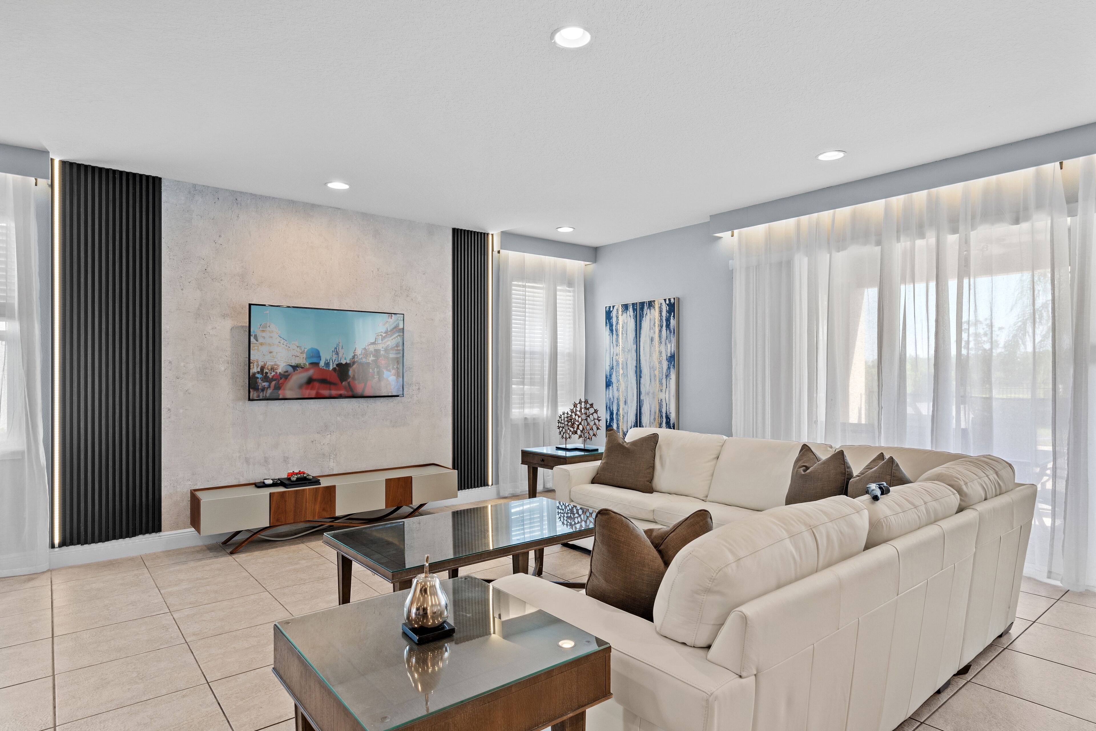 A modern living room with a sectional sofa, a glass coffee table, and a flat-screen TV mounted on the wall.