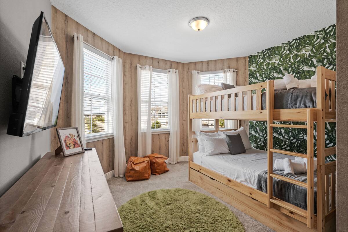 Una habitación con literas, un escritorio con un marco de fotos y un ventanal con cortinas.
