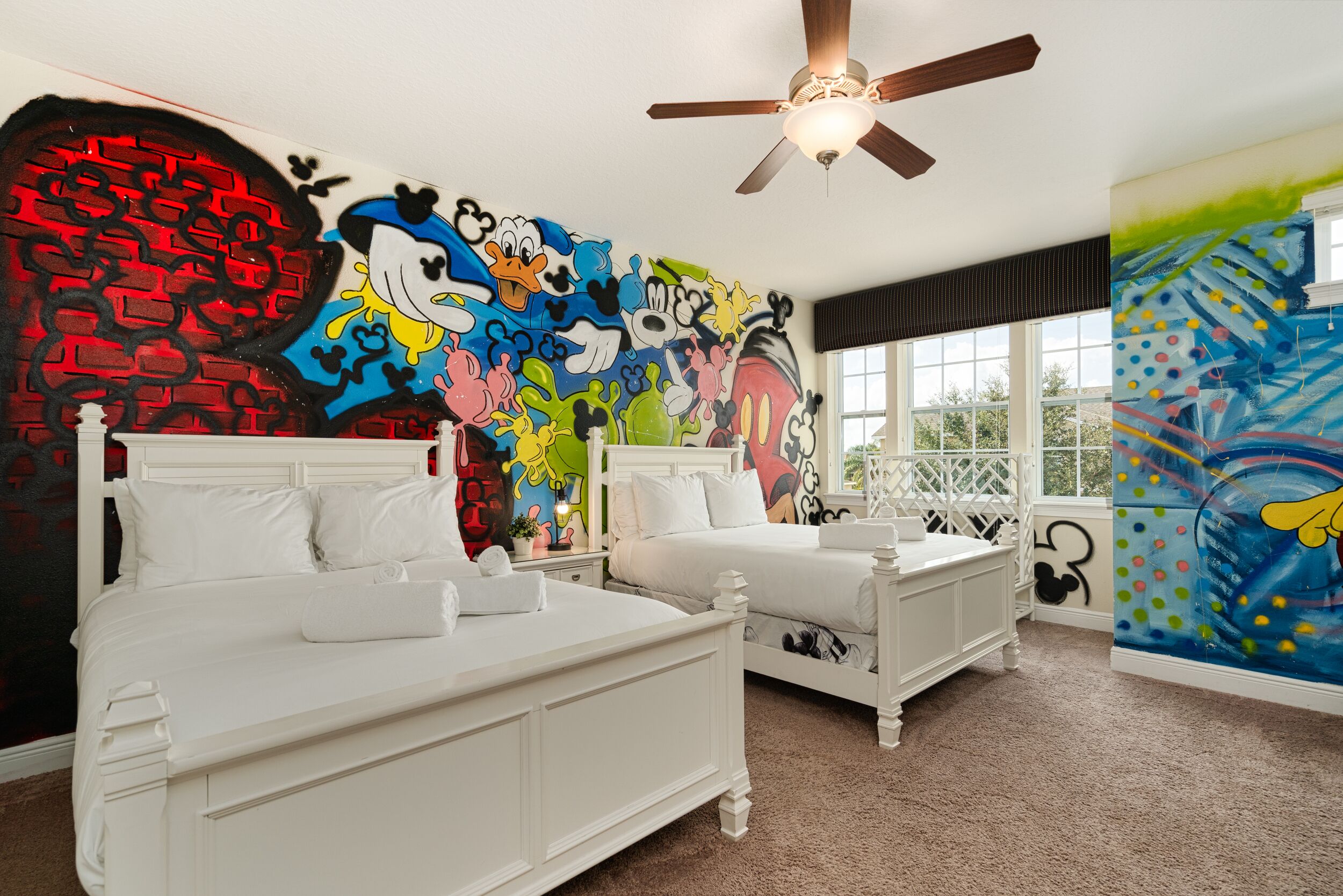 A bedroom with two white beds, a ceiling fan, and colorful graffiti art on the walls.