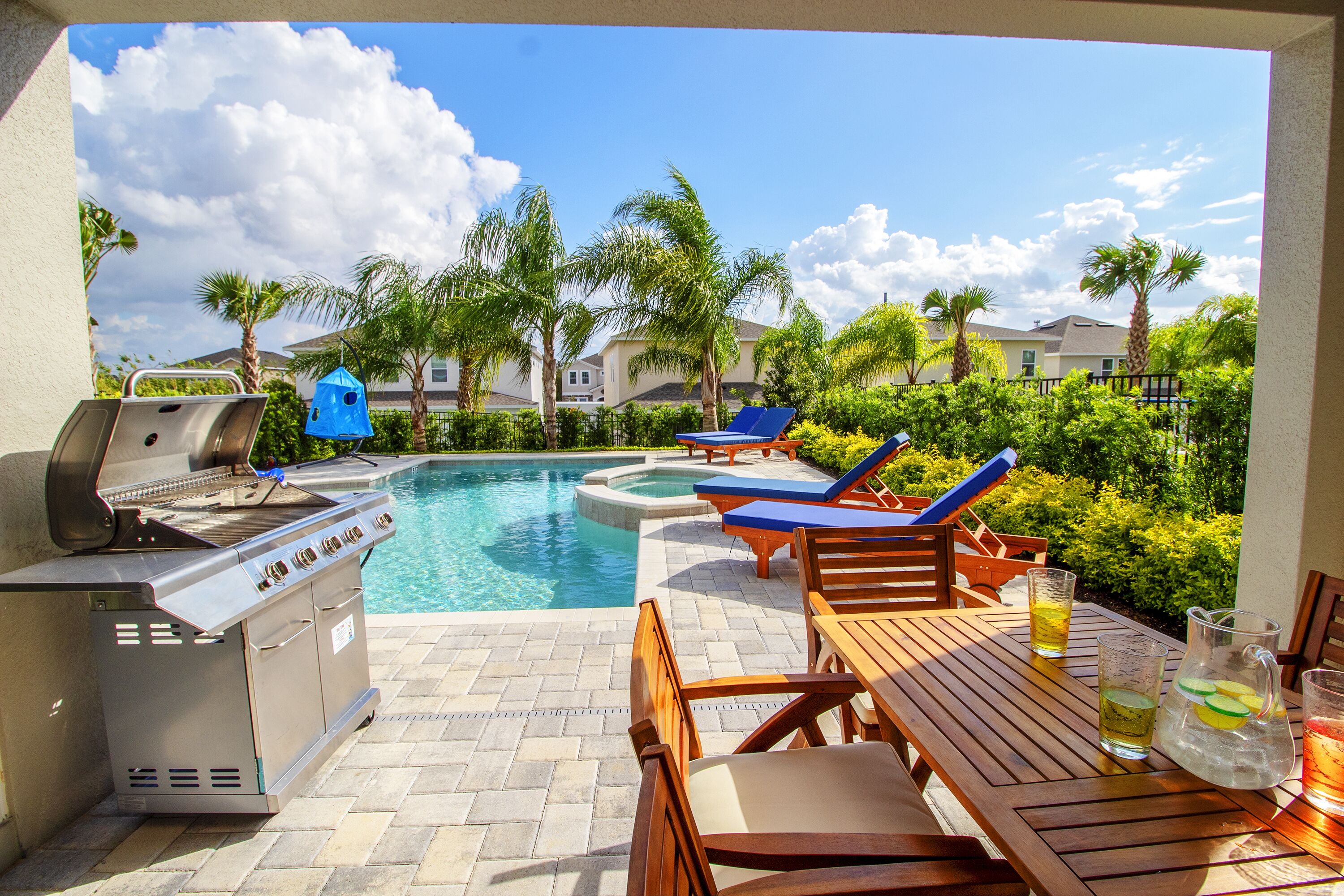 A poolside area with a grill, lounge chairs, and a table with drinks.