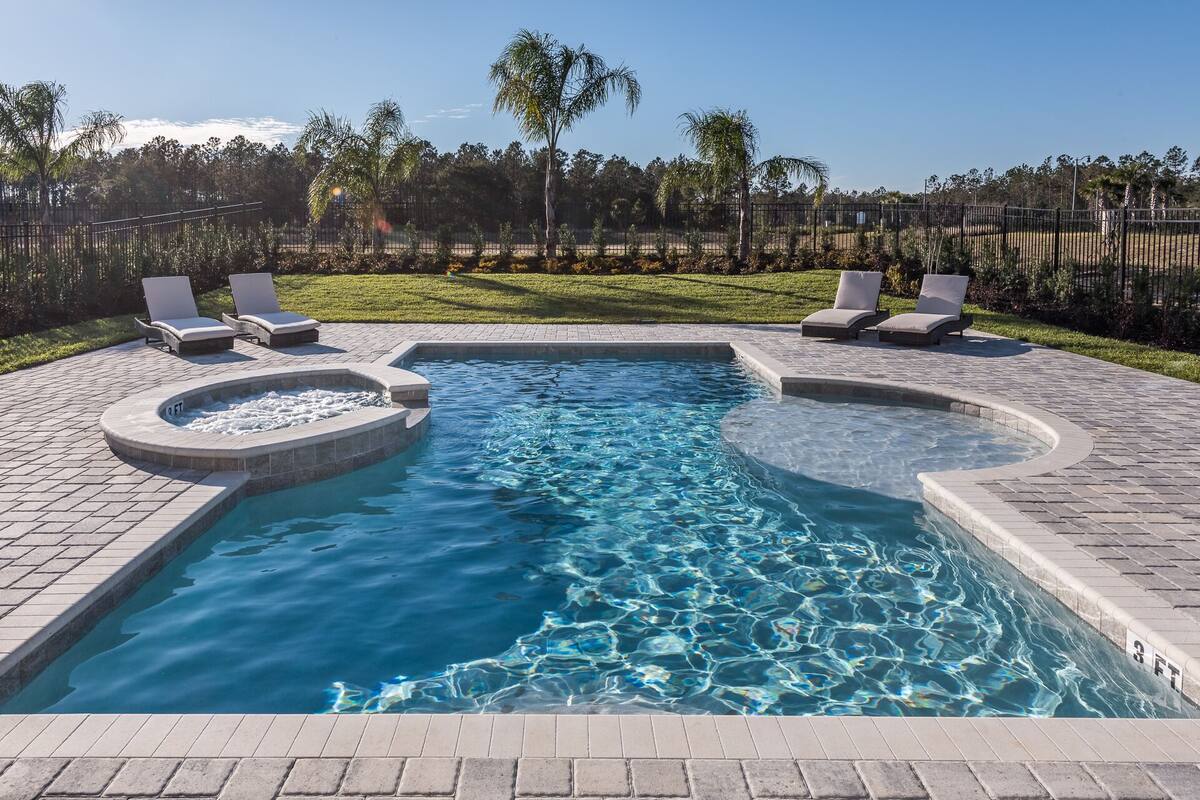 Una piscina con dos jacuzzis, rodeada por un patio empedrado y sillas de descanso.