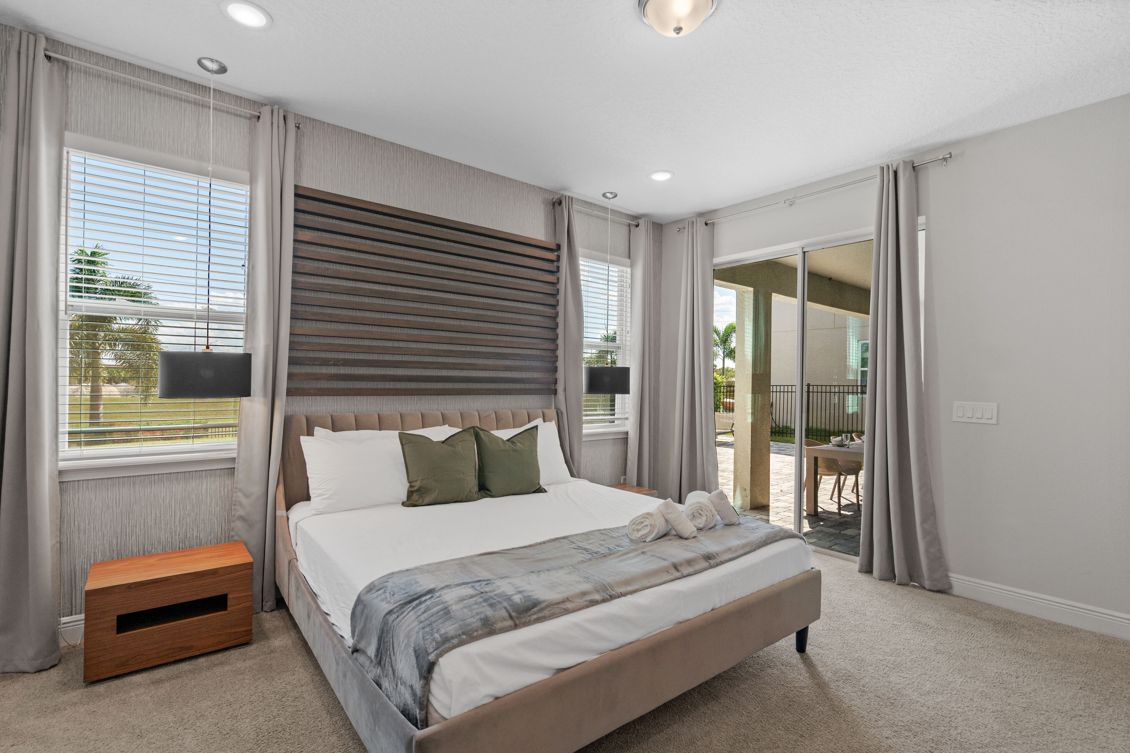 Camera da letto moderna con un letto grande, un comodino in legno e una porta scorrevole in vetro su un balcone.