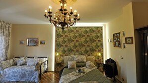Una habitación con cama, una silla, un candelabro y un muro con cuadros enmarcados.