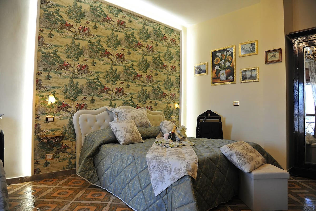 Un dormitorio con una cama, una mesita de noche, una lámpara, un aparador y una pared decorada con marcos de fotos.